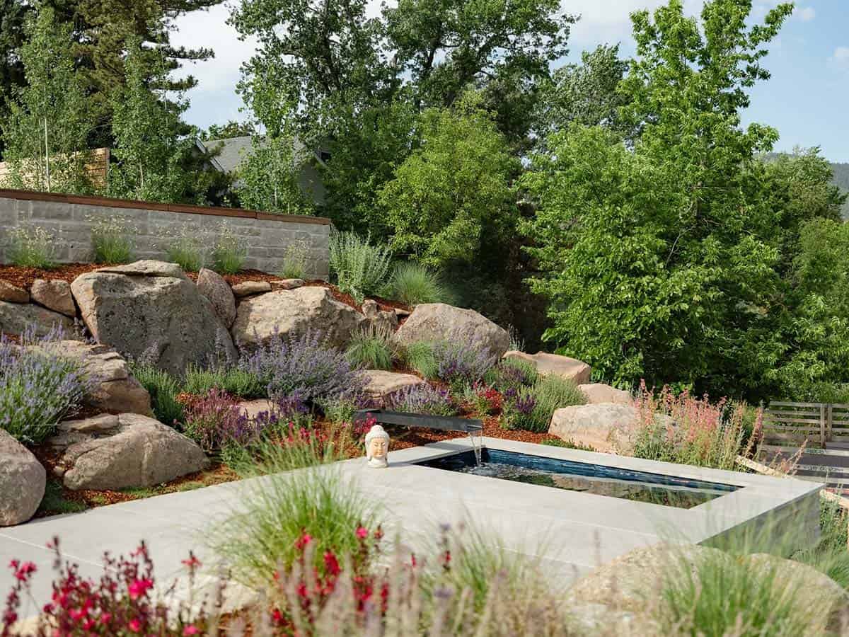 Elevated garden view of a reflecting pool, boulders, lavender, and a small Buddha statue at sunset