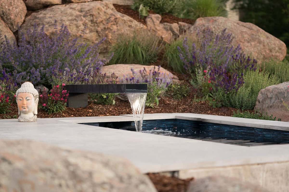 Close-up of a spillway water feature flowing into a dark-tiled pool framed by lavender and a Buddha figure