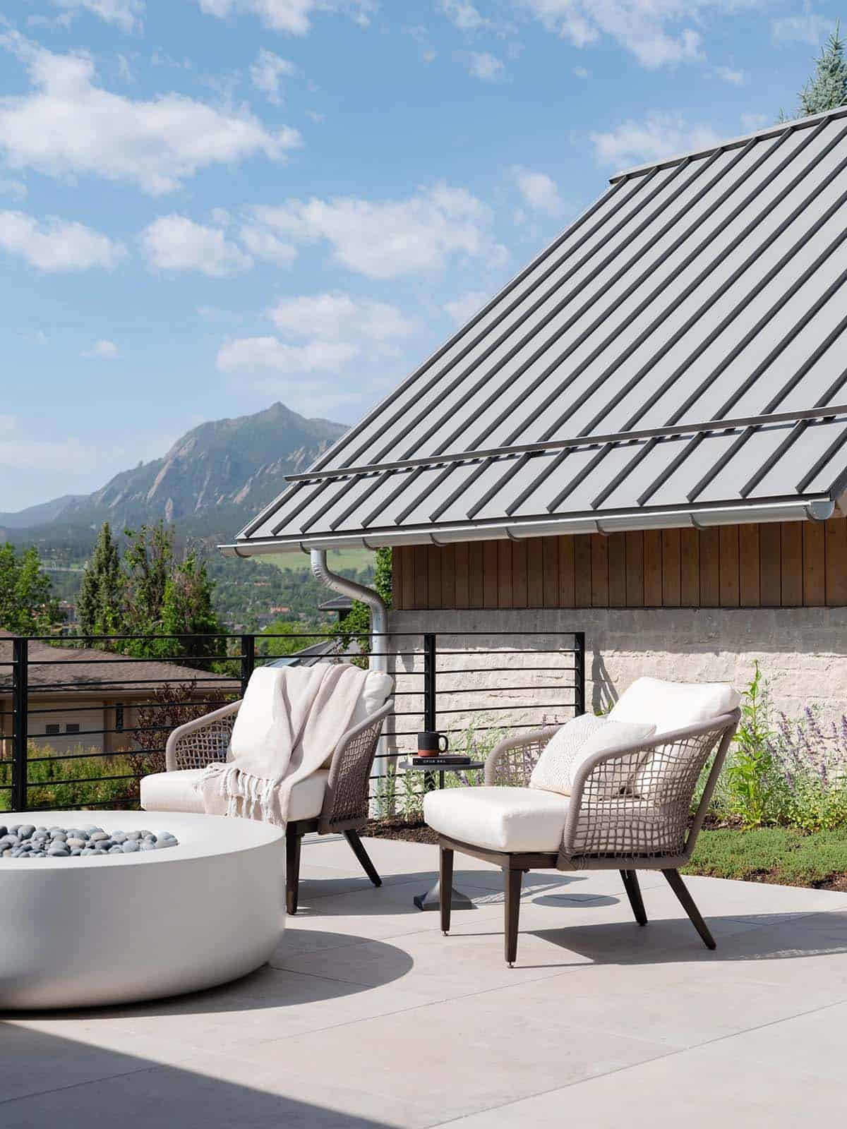 Rooftop lounge chairs with cushions and throws beneath a slanted metal roof overlooking the Flatirons