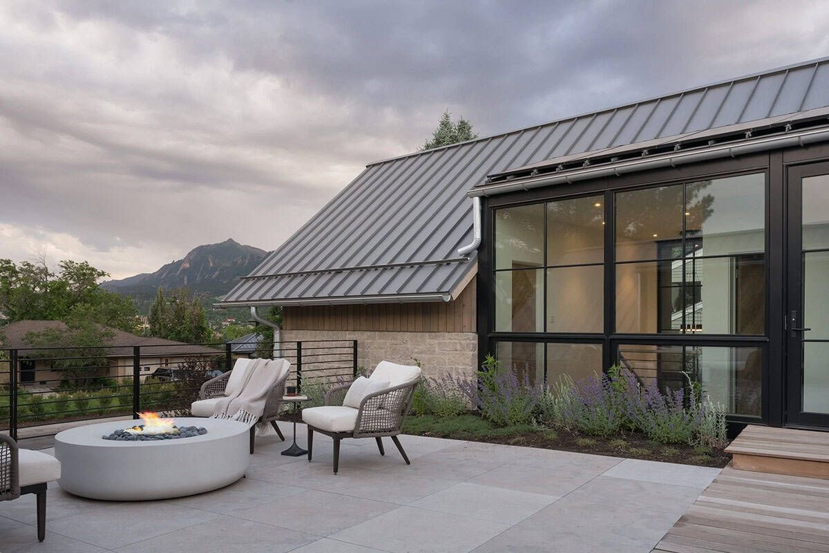 Evening rooftop terrace with fire bowl, lounge chairs, and glass-walled addition under a moody sky