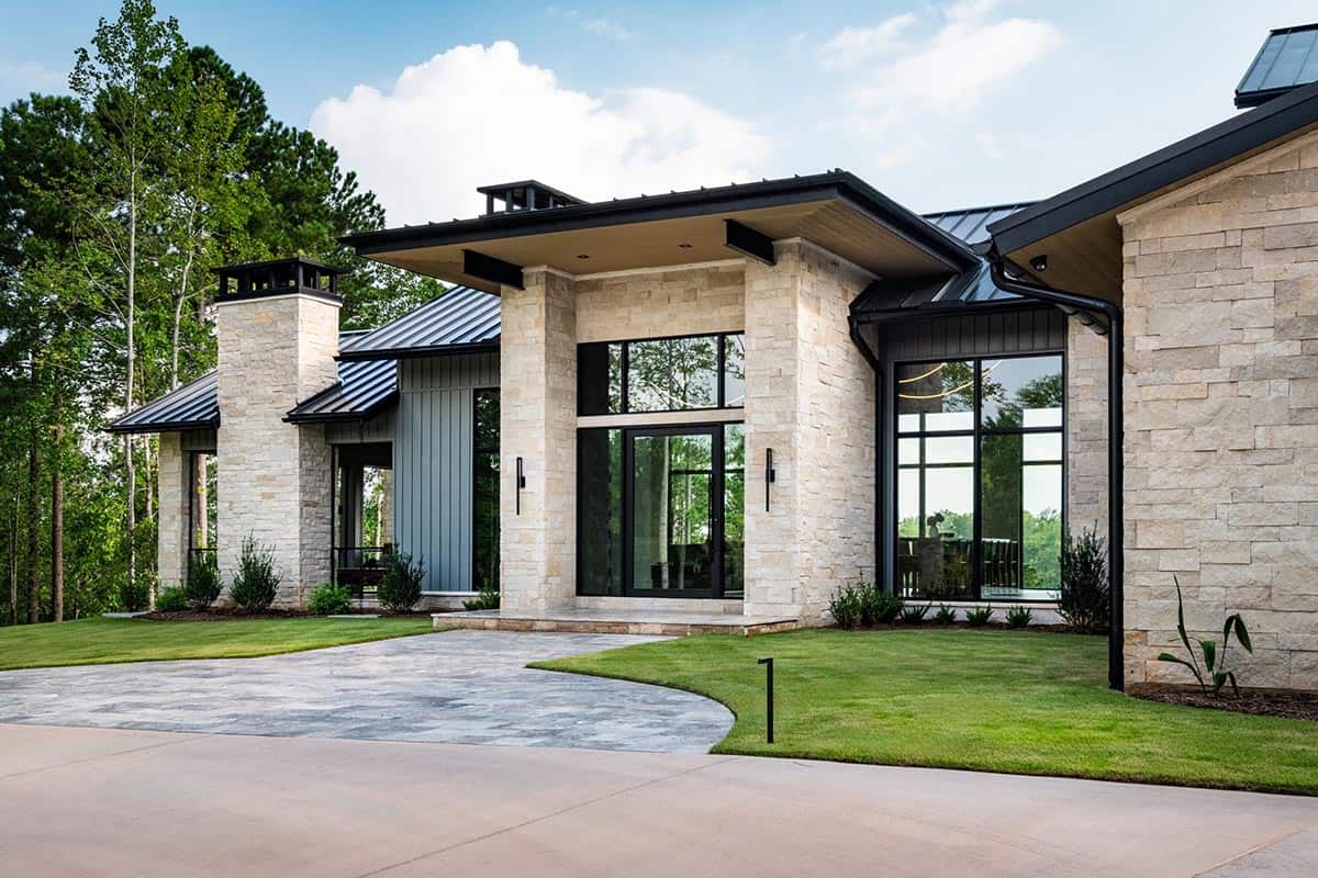Modern lake house entrance with stone columns, tall glass front door, and metal roof
