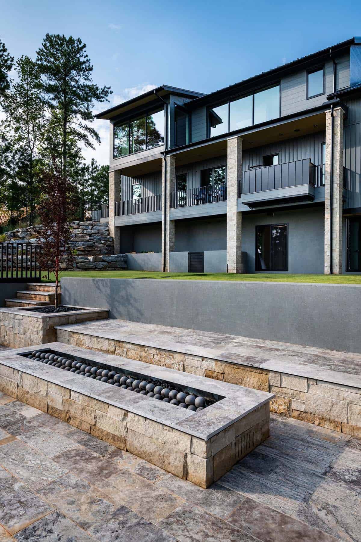 Stacked stone patio with linear fire pit and tiered retaining walls behind home