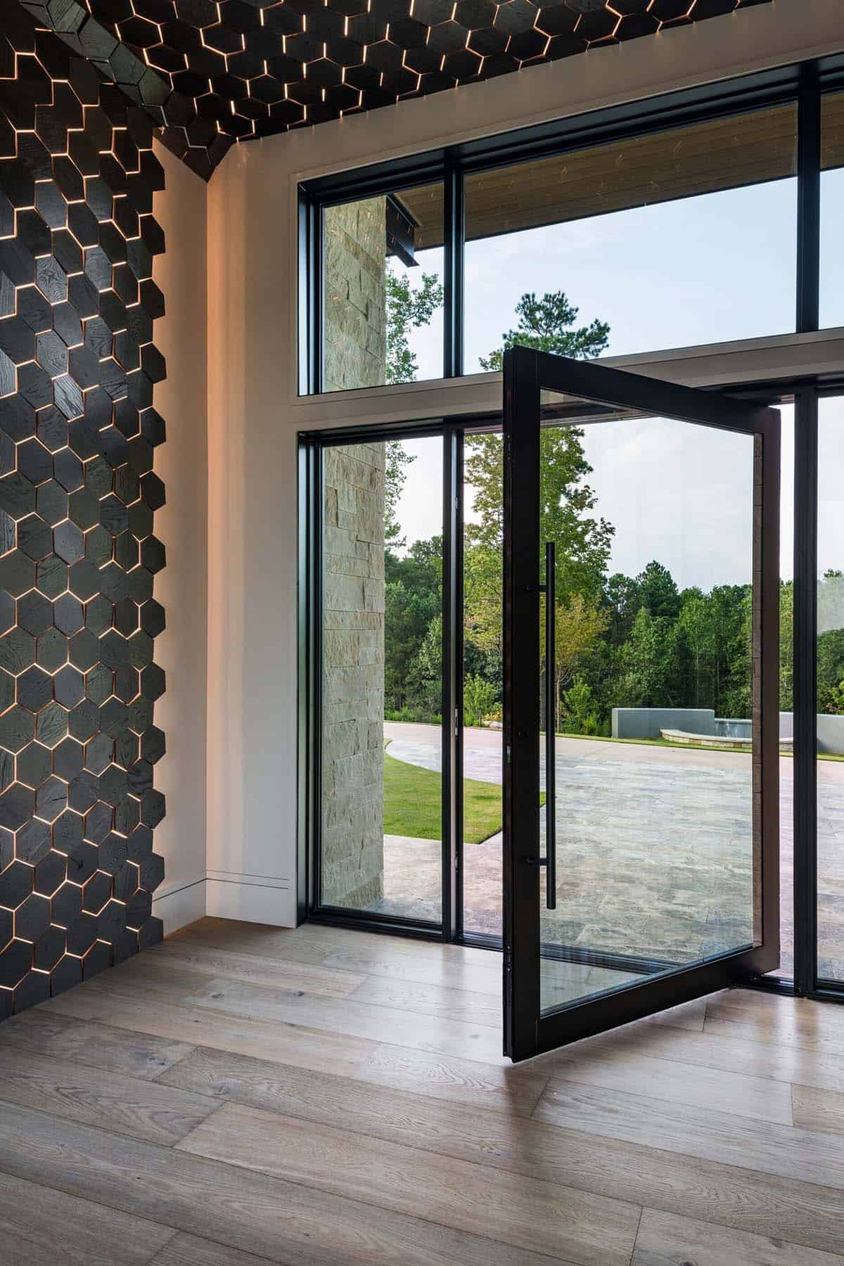 Black hexagonal wood-paneled entryway with glass pivot door and forest view
