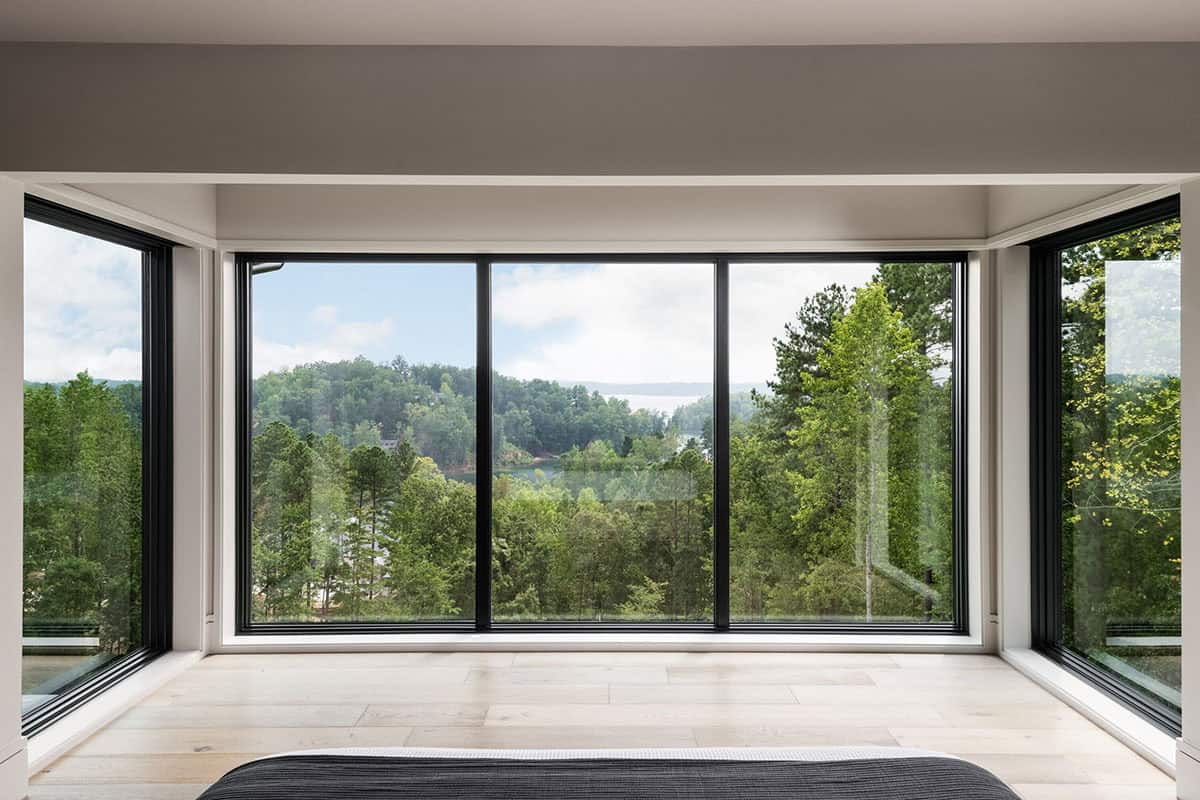 Floor-to-ceiling corner windows overlooking lake and tree canopy
