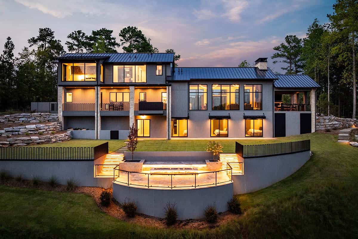 Rear exterior of lake house at twilight with illuminated windows and stone terracing