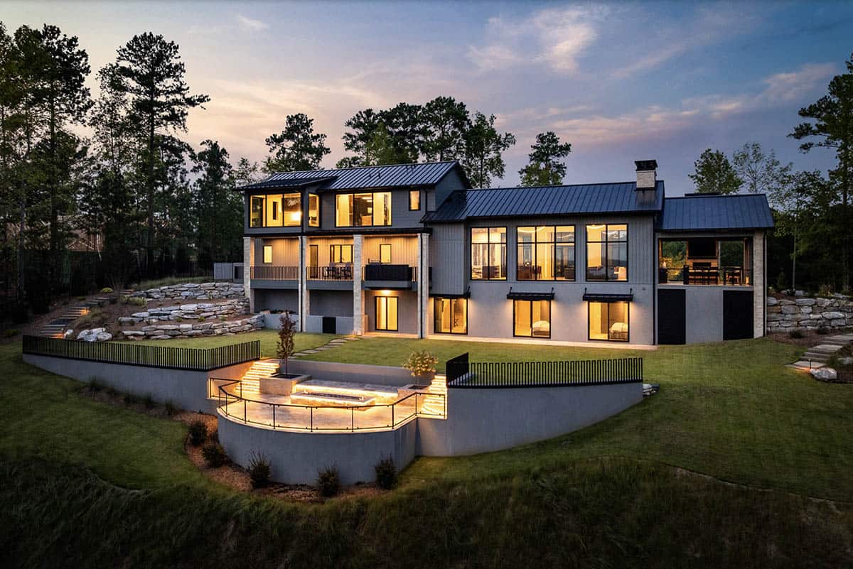 Rear exterior at dusk with illuminated rooms and curved terrace fire feature