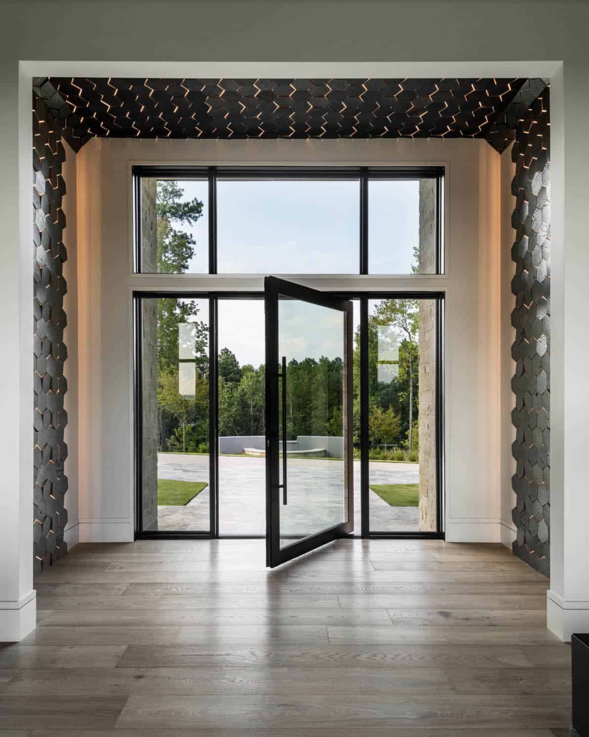 Foyer with hexagonal wood accent walls framing glass pivot door and lake-view driveway