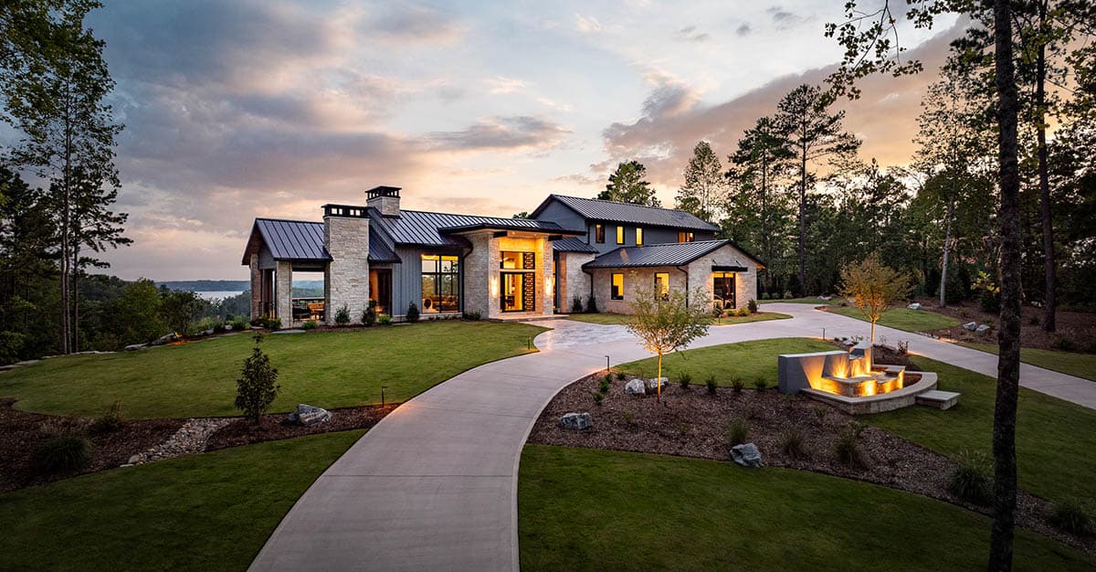 Front exterior at sunset with stone chimney, covered entry, and tiered fire pit