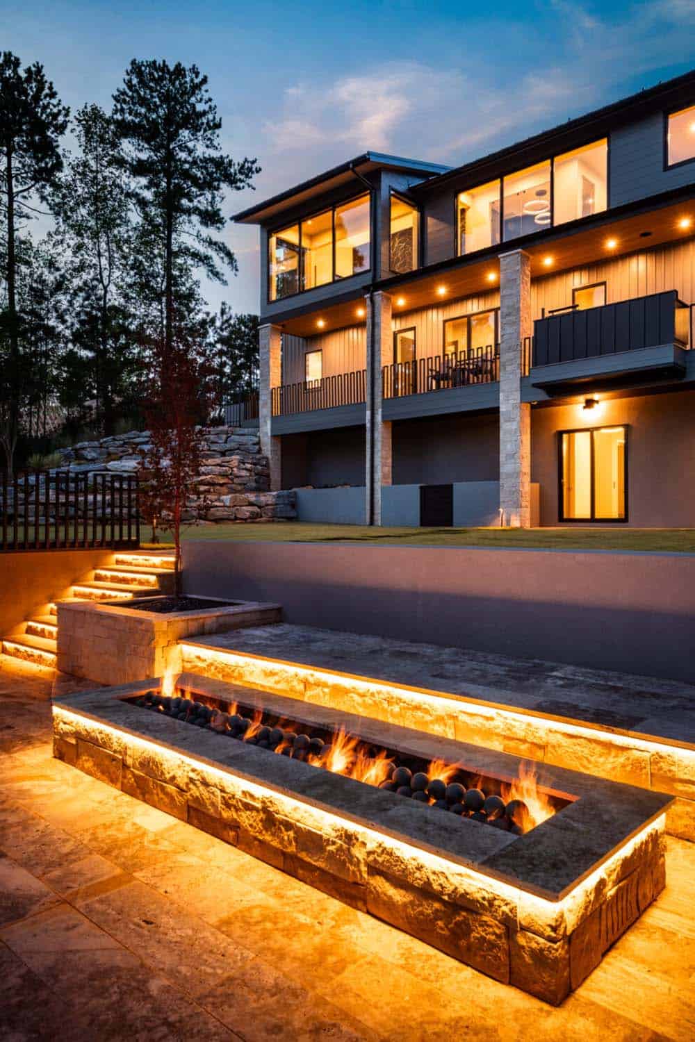 Multi-level rear terrace with stacked stone steps and linear fire pit at dusk