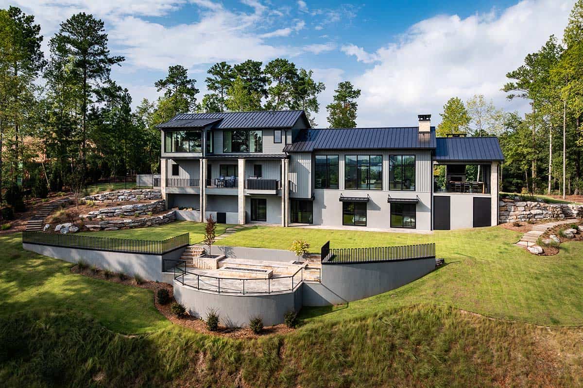Rear exterior with stone retaining walls, terraced lawn, and curved patio