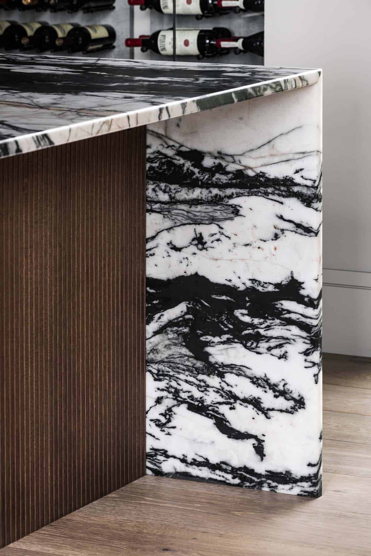 Detail of veined marble countertop against ribbed wood cabinetry near wine wall