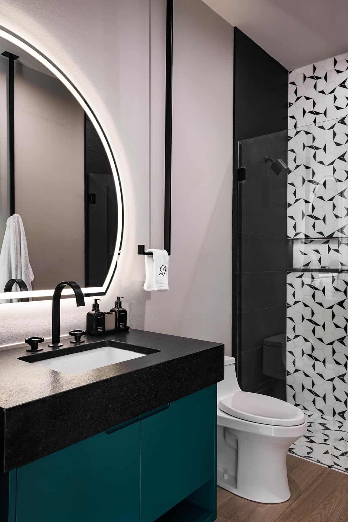 Teal vanity bathroom with round backlit mirror and patterned tile shower