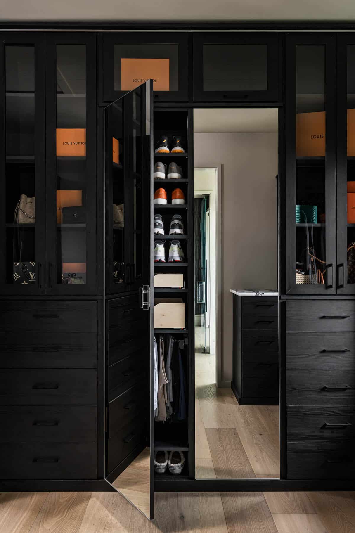 Walk-in closet with black cabinetry, glass-front shelving, and designer handbag display