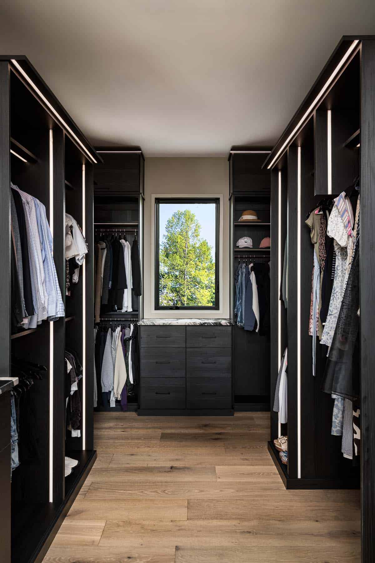 Walk-in closet with backlit shelving, center dresser, and tree-framed window