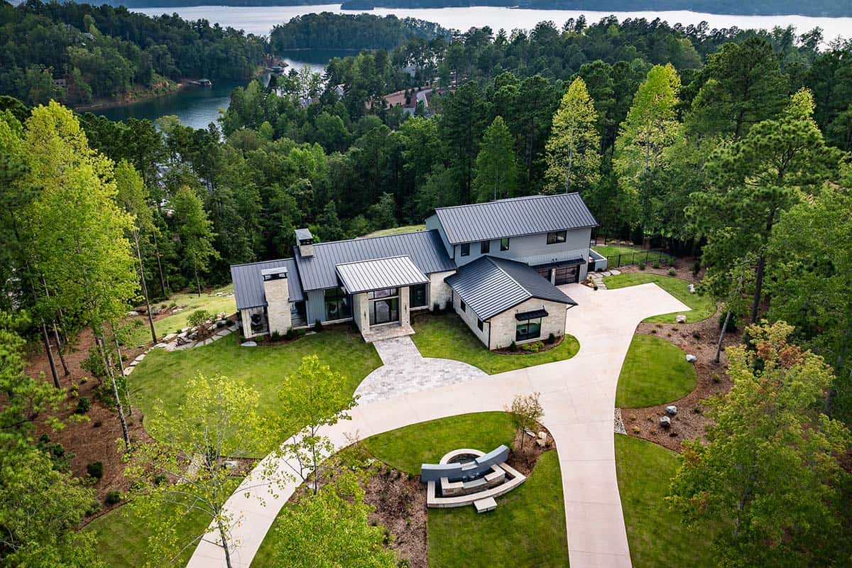 Aerial view of lake house surrounded by forest with winding driveway
