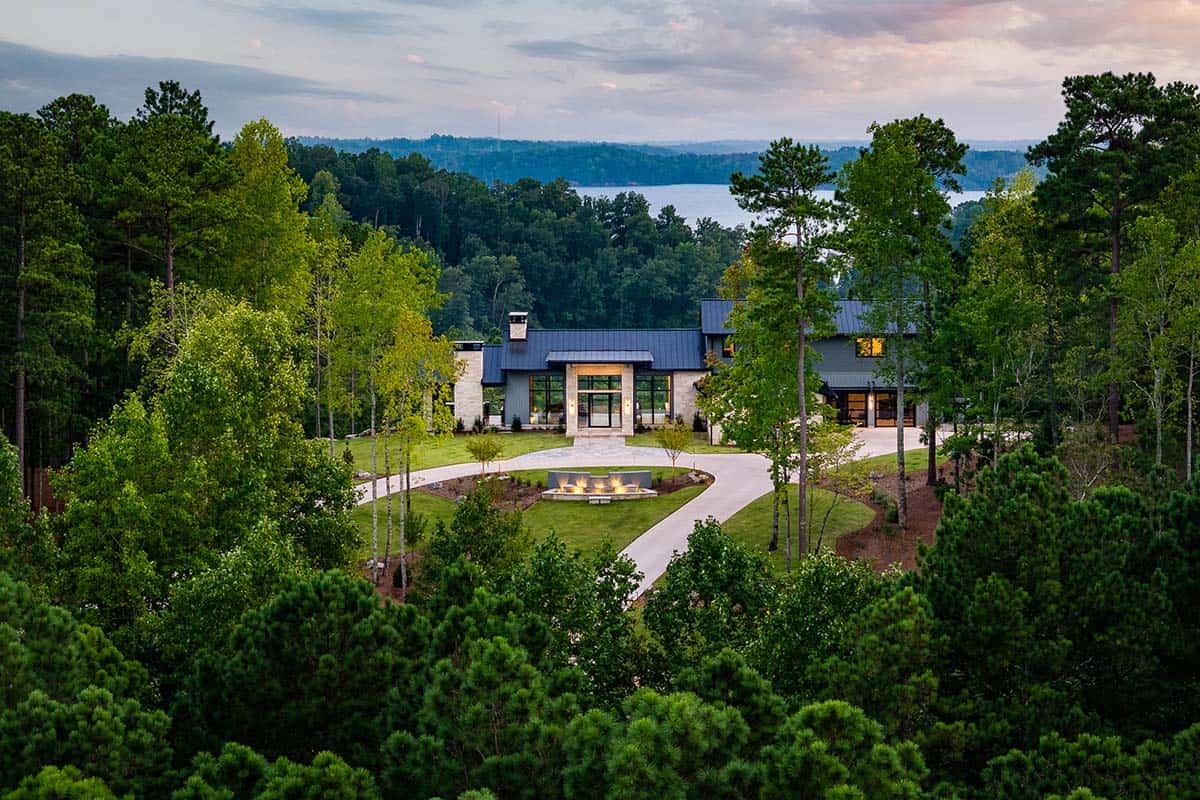 Aerial dusk view of home nestled in pines with distant lake backdrop