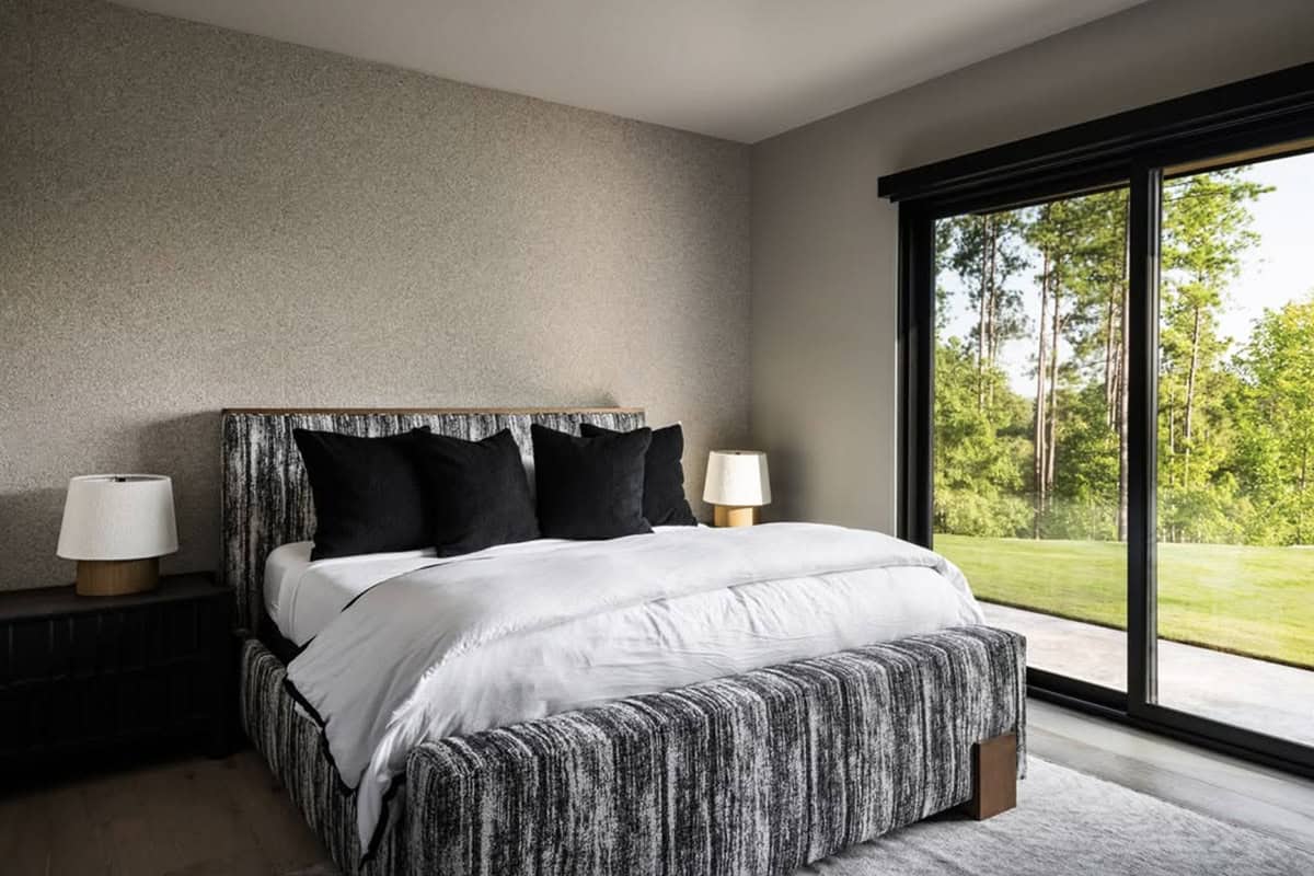 Bedroom with striated upholstered bed, black throw pillows, and forest-view sliding door