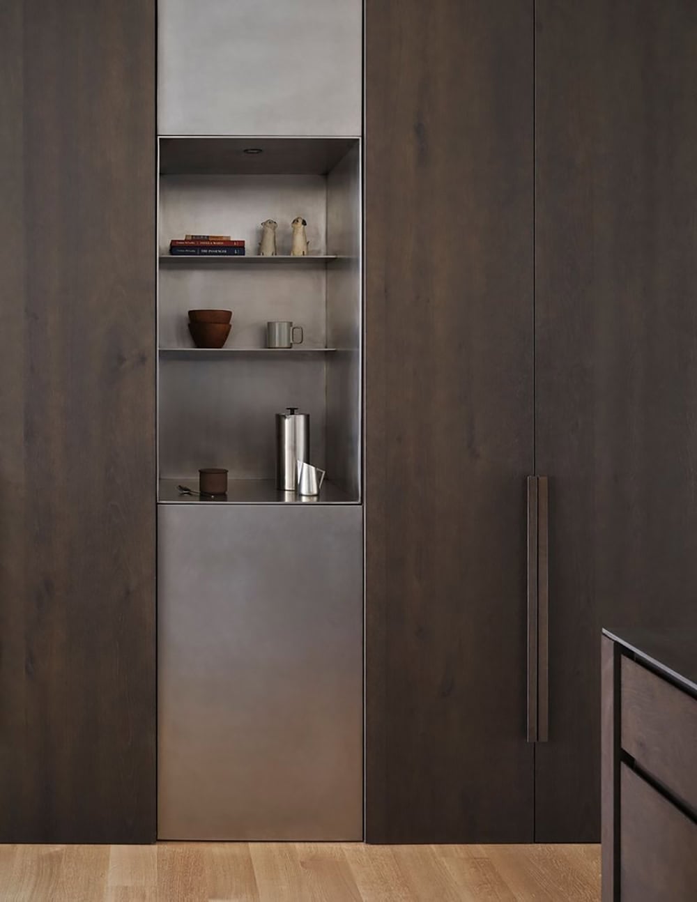 Detail of steel-lined built-in shelving niche with books and ceramics in dark wood wall