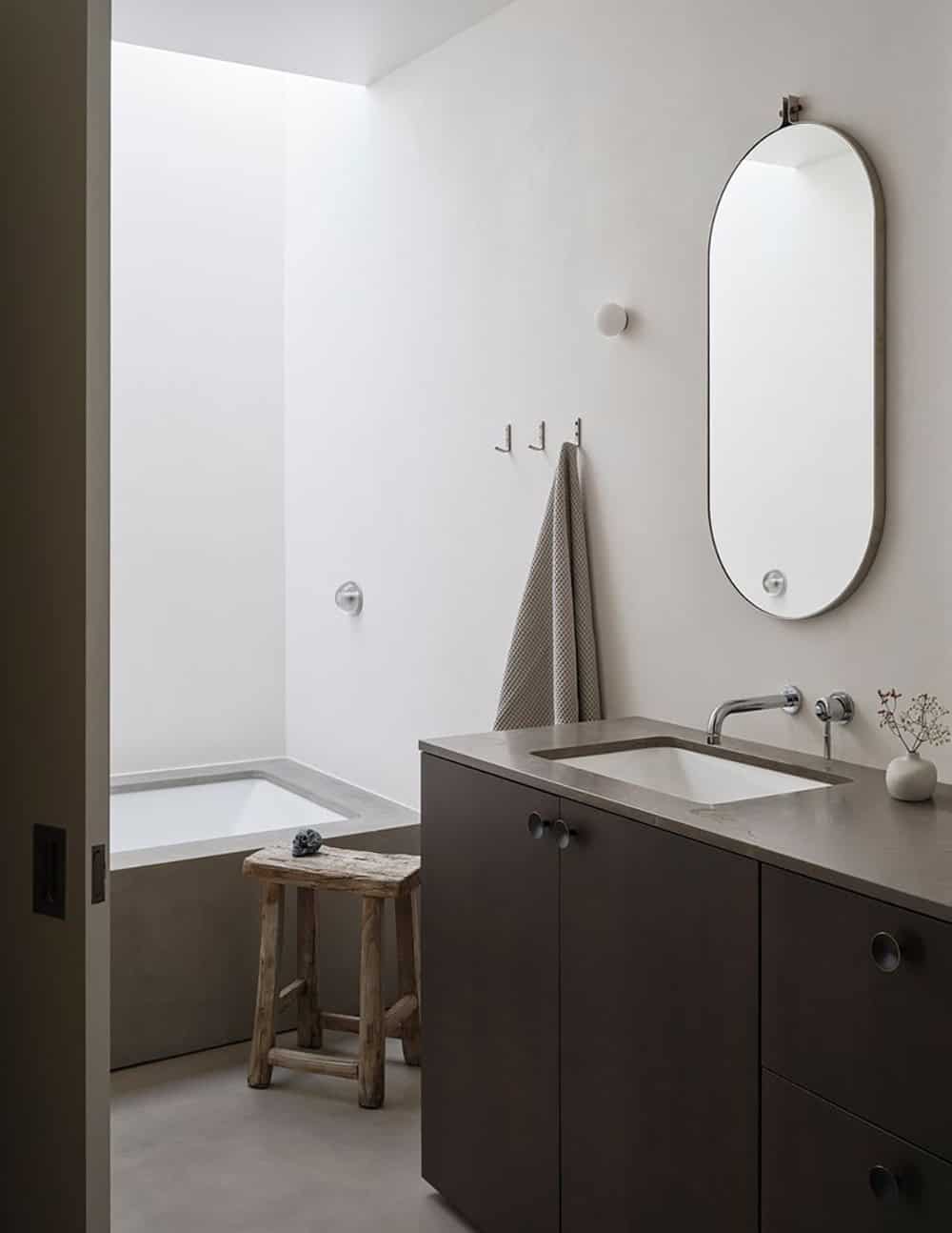 Primary bathroom with concrete soaking tub, dark vanity, oval mirror, and perimeter skylight