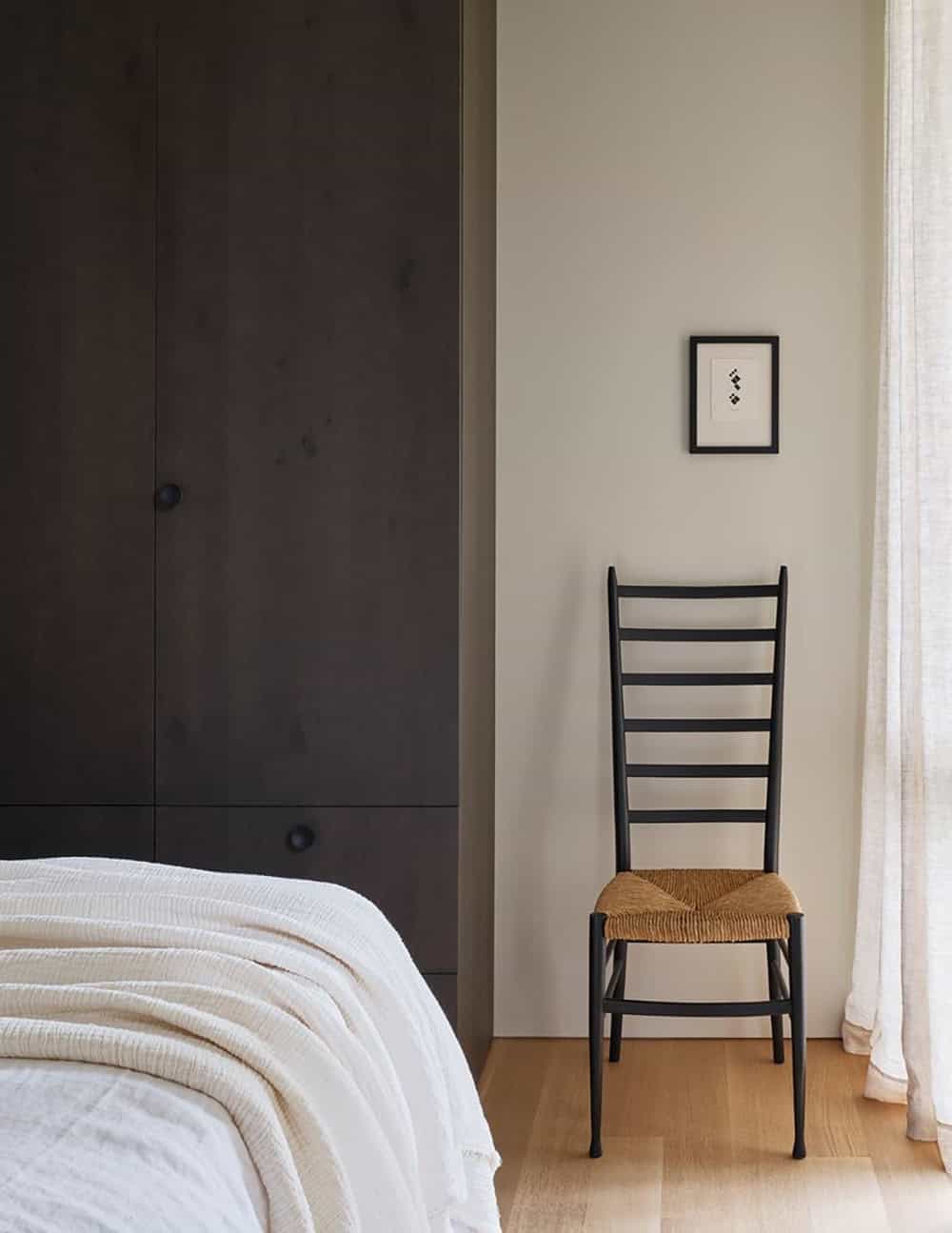 Bedroom corner with dark wood wardrobe, tall ladder-back chair, and small framed artwork