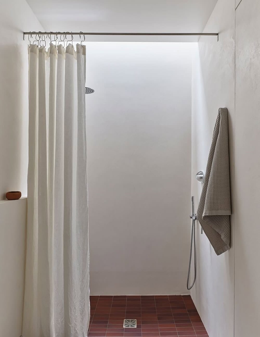 Shower with linen curtain, terracotta tile floor, and skylight above