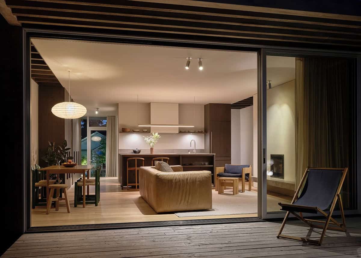 Night view through open sliding doors into the warm, lit living and dining area