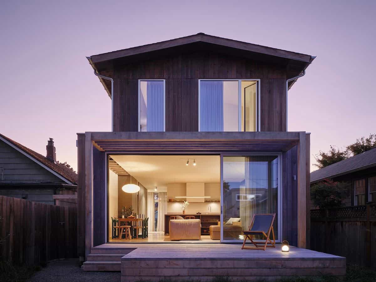 Rear exterior at dusk with cedar siding, open sliding doors, and glowing interior
