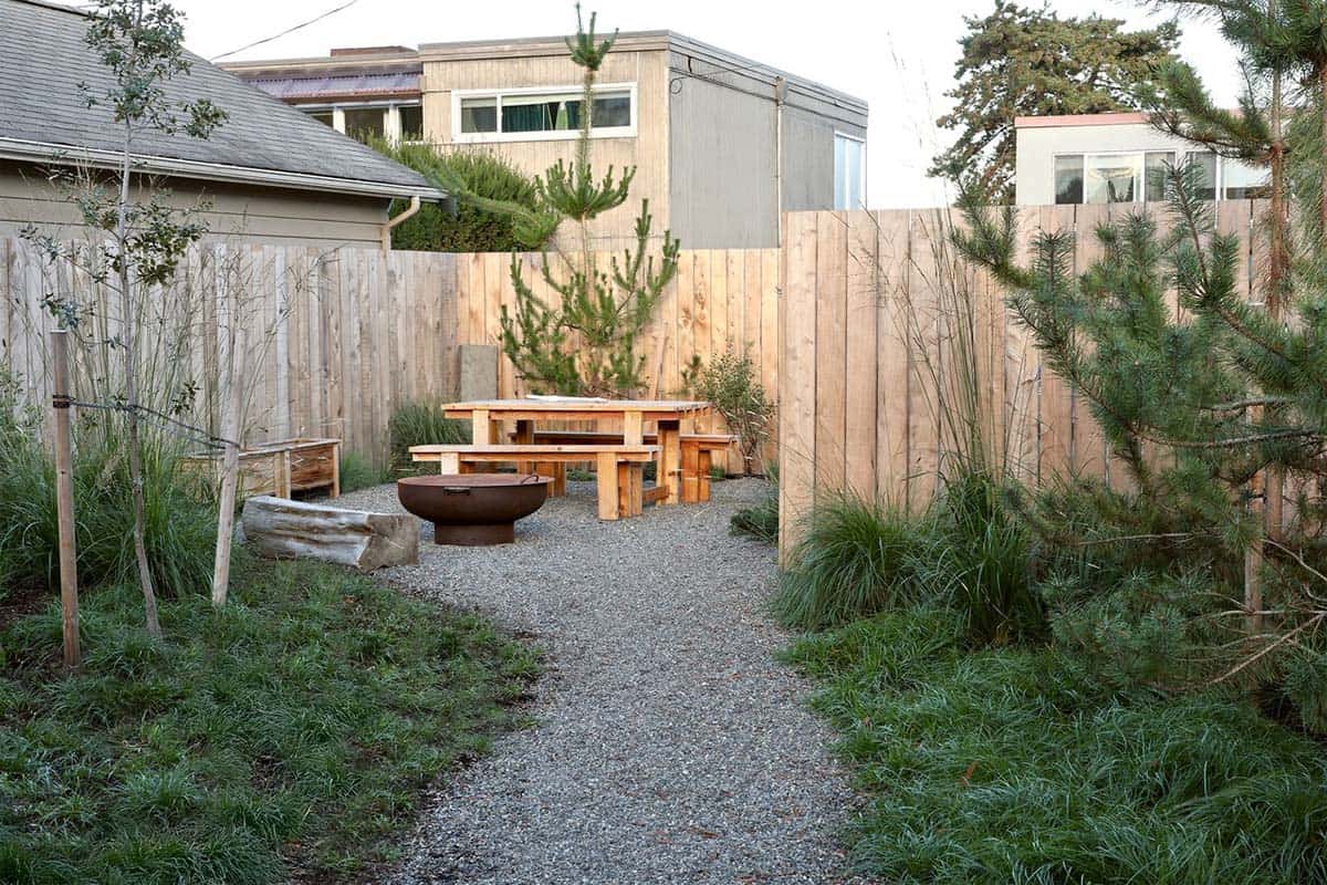 Backyard gravel garden with wood picnic table, fire bowl, and young pine trees