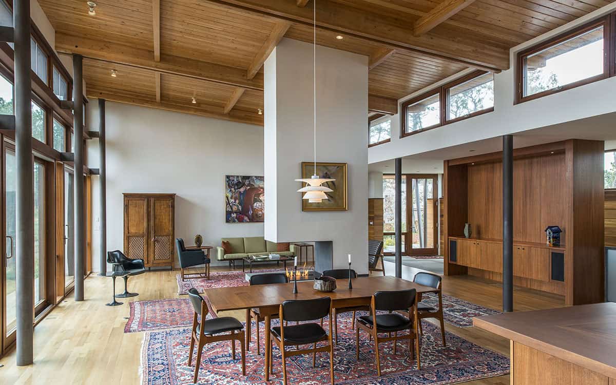 Great room dining area with exposed wood beam ceiling, walnut dining table, pendant light, Persian rug, and view into the wood-paneled hallway