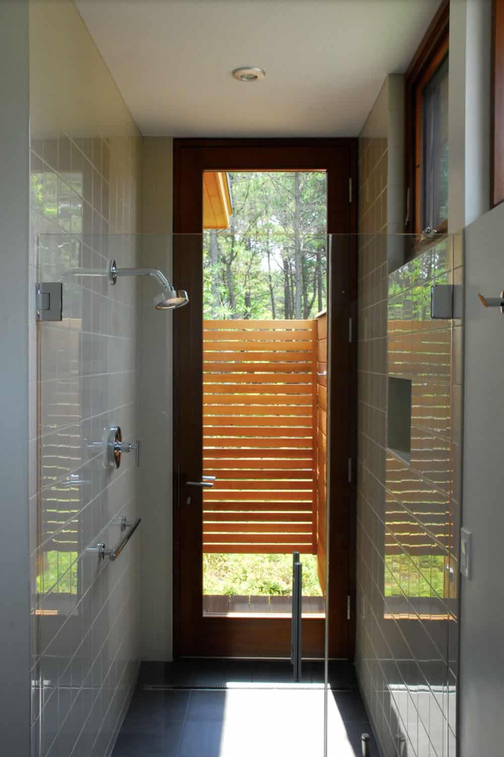 Tile-walled shower with dual showerheads and a wood-framed door with horizontal slatted screen opening to a private outdoor area
