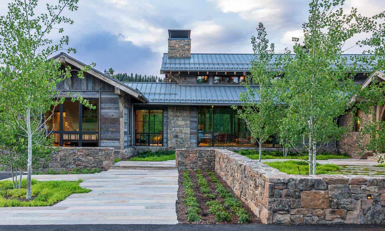 Modern alpine home exterior with stone walls, reclaimed wood siding, and metal roof at dusk