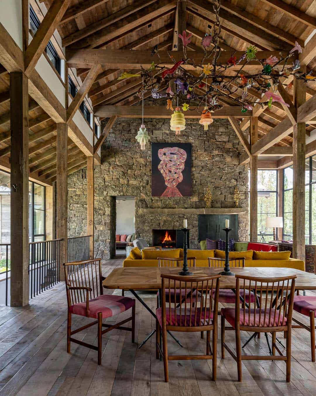 Great room with vaulted timber frame, stone fireplace, and colorful glass chandelier