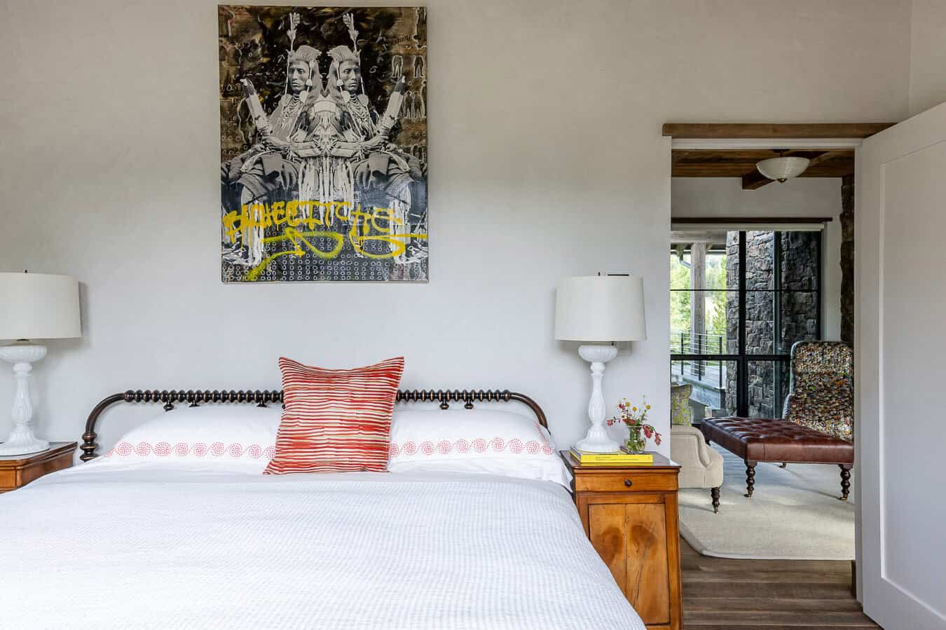 Guest bedroom with spindle bed, art above headboard, and view into en suite bath
