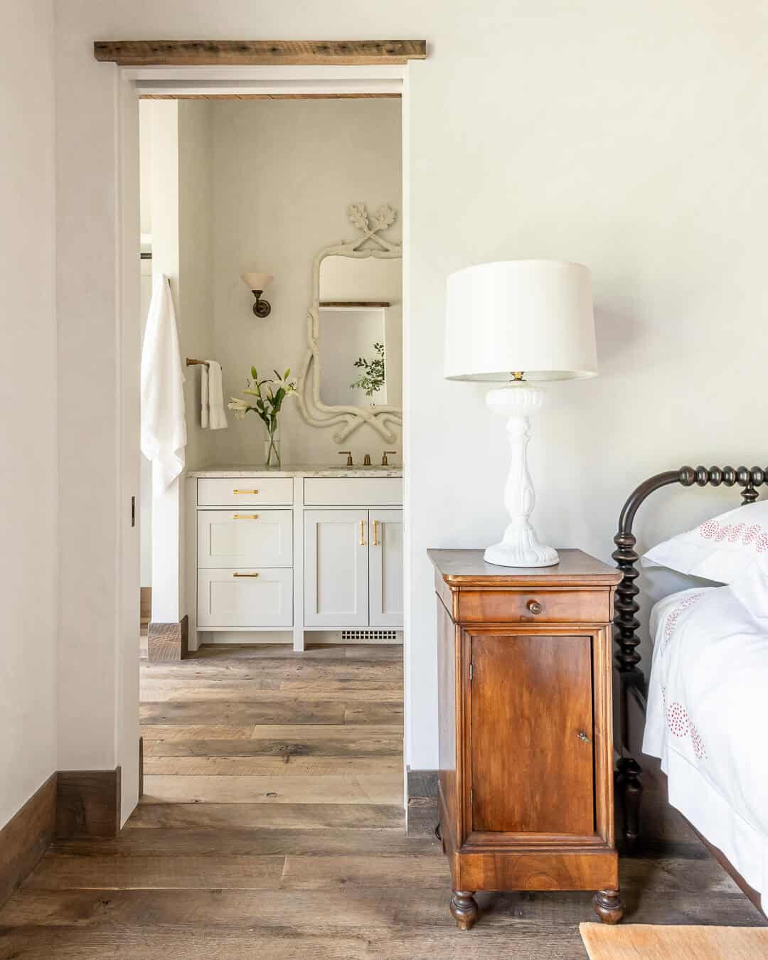 Guest bedroom with spindle bed and nightstand opening to white en suite bathroom