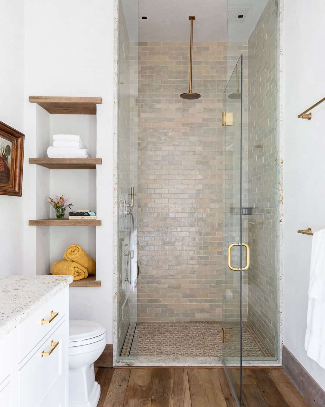 White en suite bathroom with marble shower, brass fixtures, and wood shelving