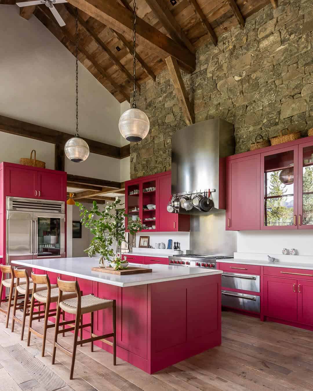 Kitchen island with raspberry cabinets, stone wall, and soaring timber ceiling