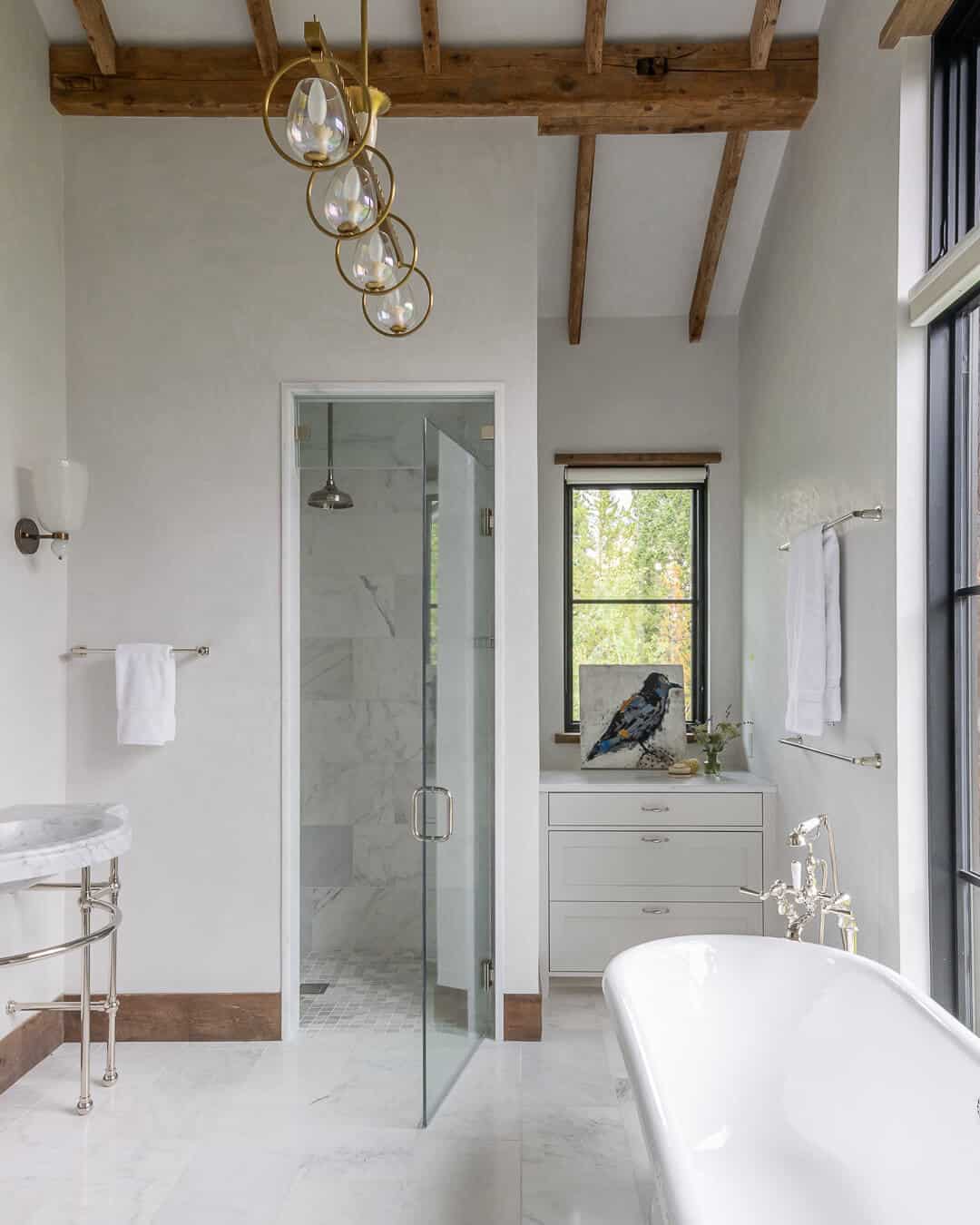Primary bath with freestanding tub, marble shower, gold chandelier, and timber beams