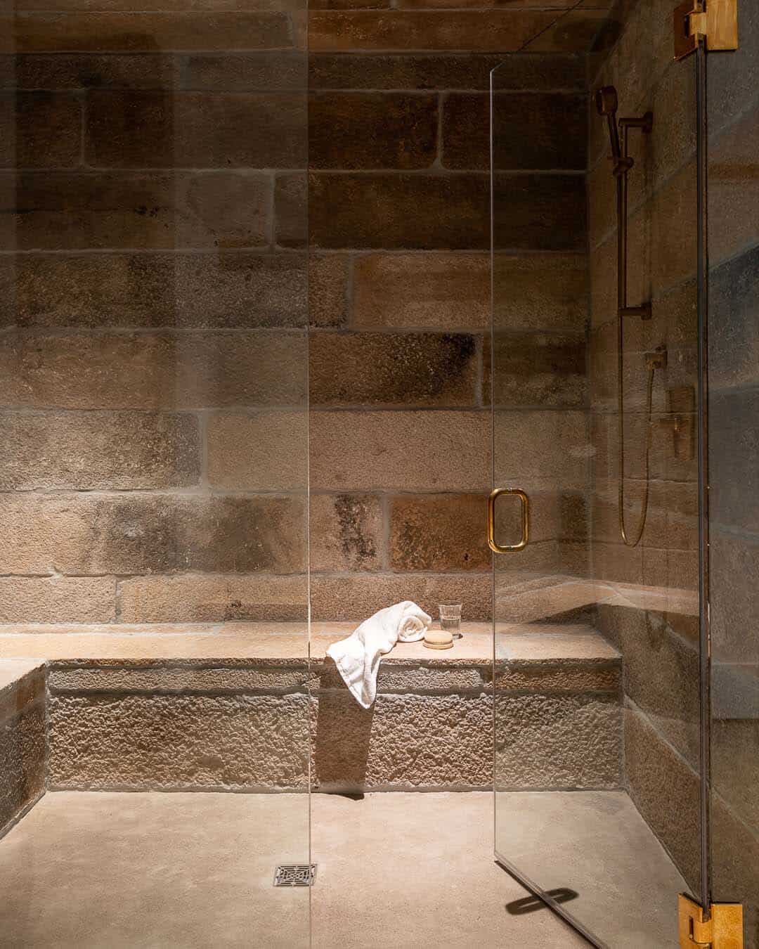 Walk-in shower with rough-cut stone walls, built-in bench, and brass fixtures