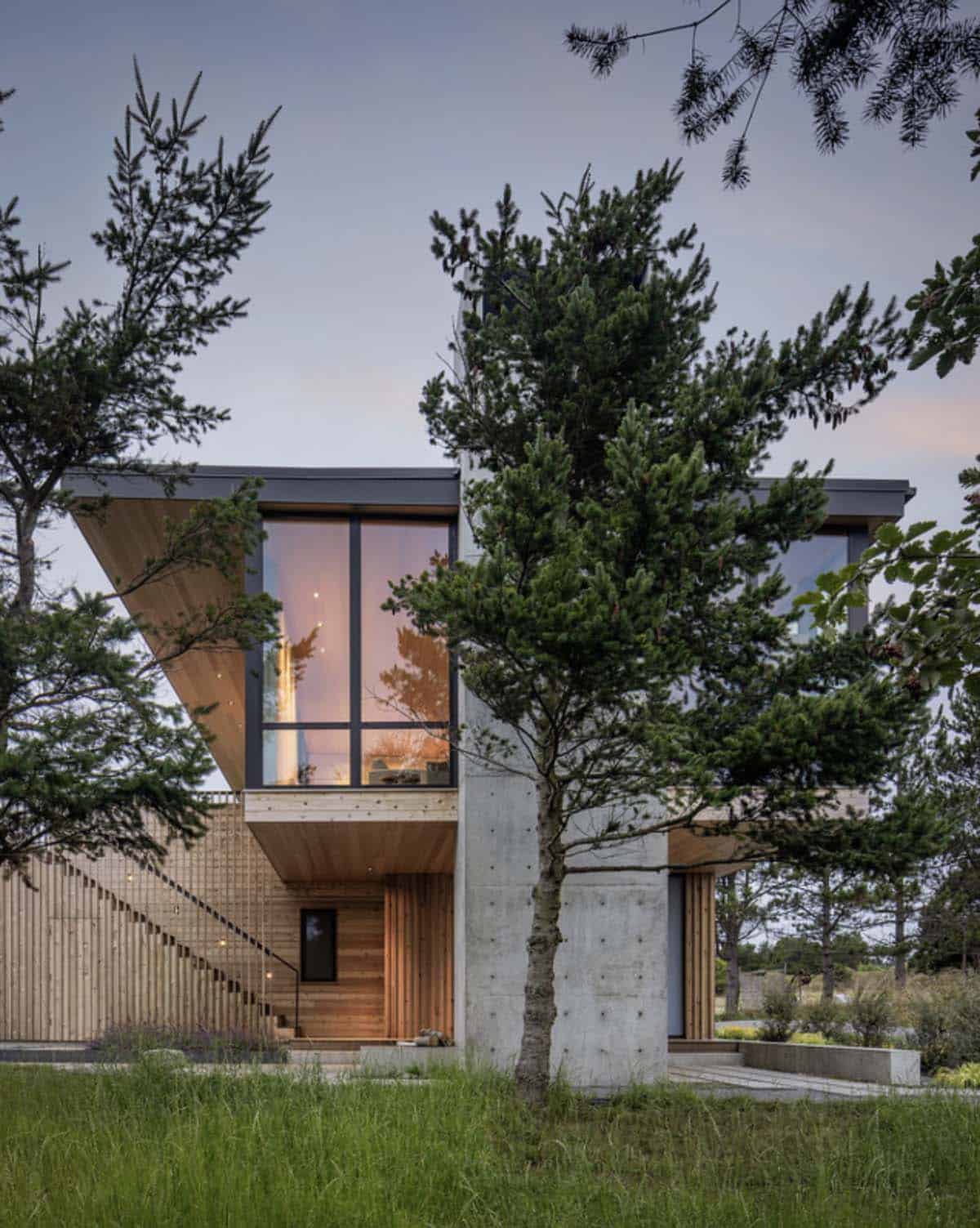 Dusk view of the home's angled cedar overhang and concrete tower framed by a young pine tree