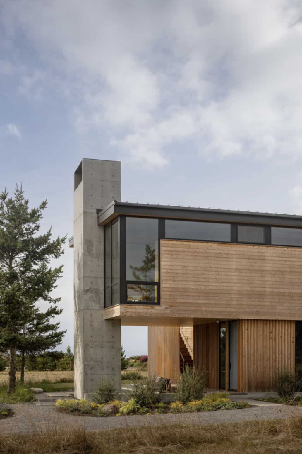 Close-up of the board-formed concrete chimney and cantilevered cedar volume against a cloudy sky