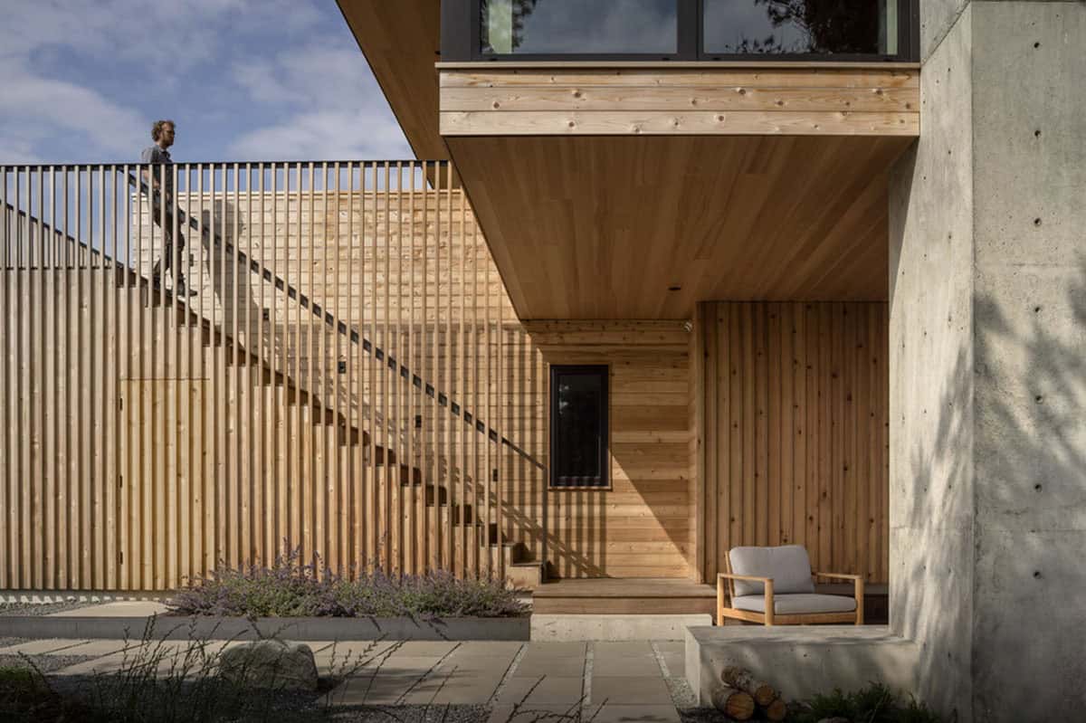 Open-air cedar slat staircase leading to the upper deck, with a person walking down and an outdoor armchair below