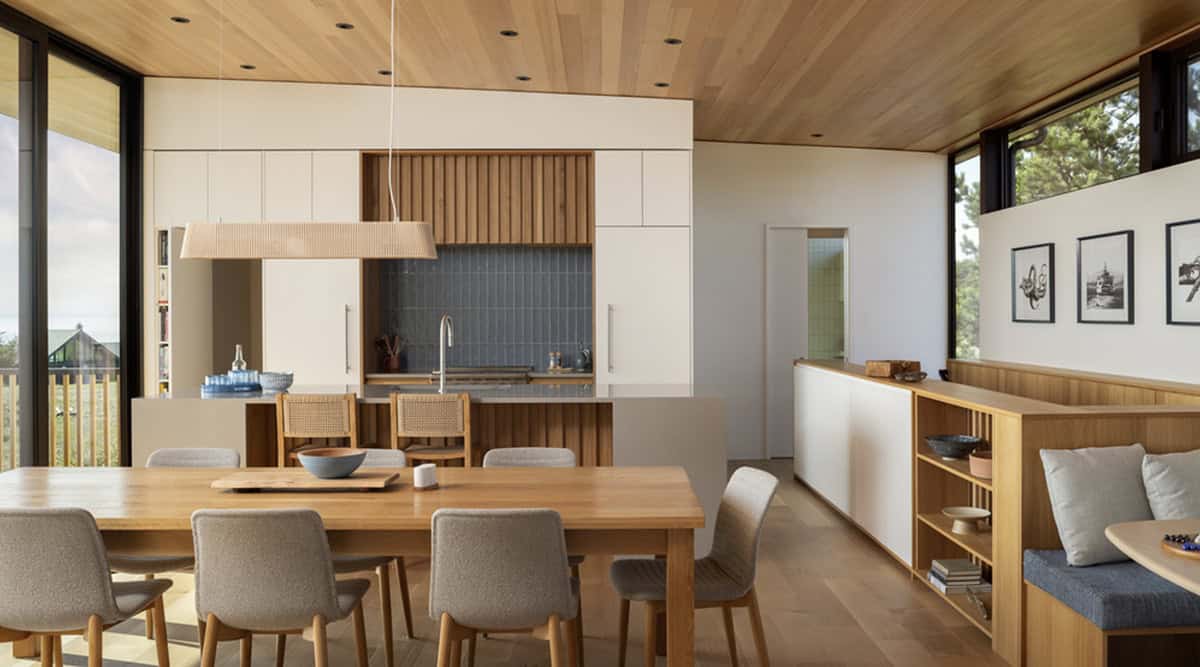 Open-concept dining and kitchen area with a wood-paneled ceiling, white cabinetry, and ocean-view windows