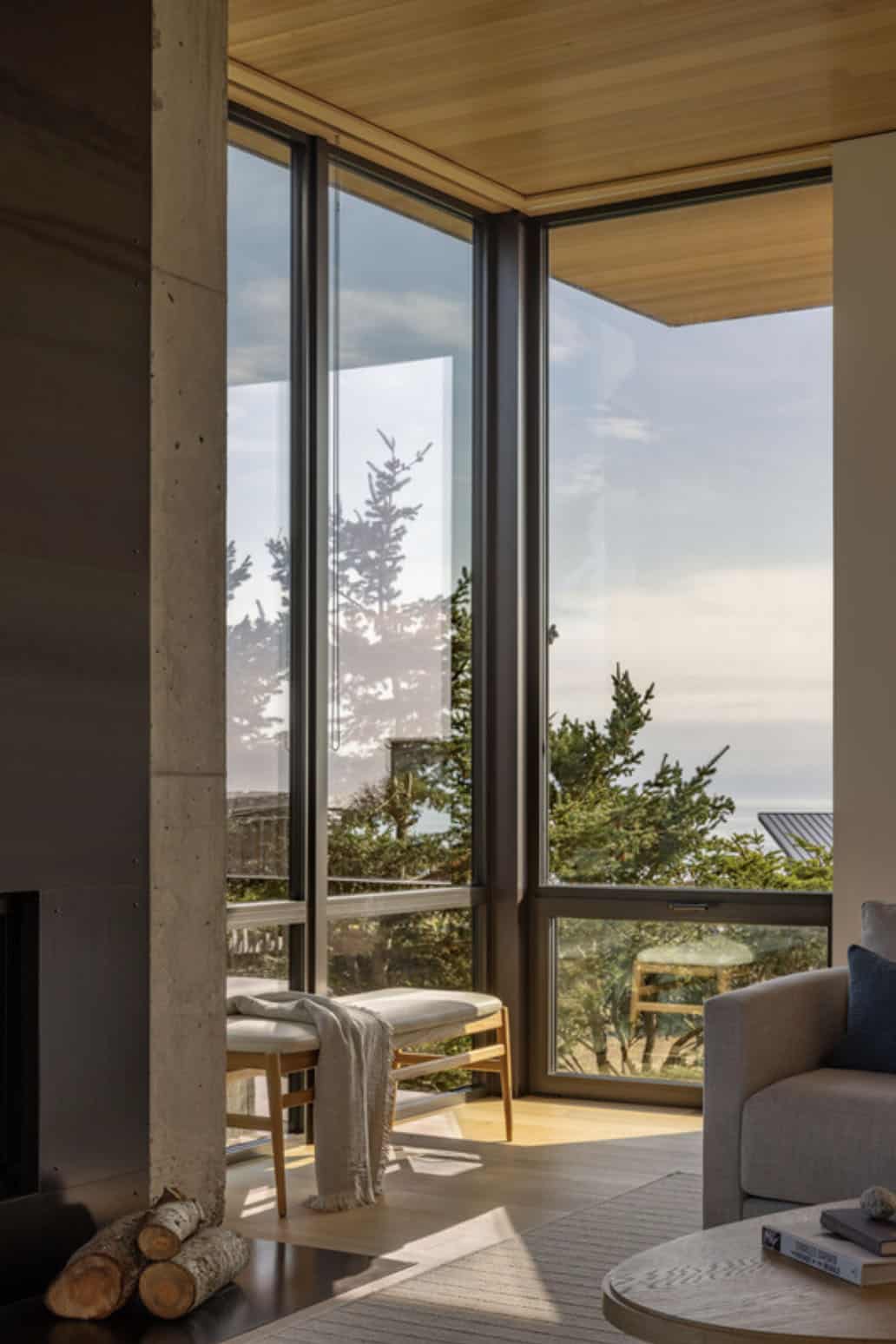Corner window nook with a wooden bench seat, cushions, and a stacked firewood pile beside the fireplace
