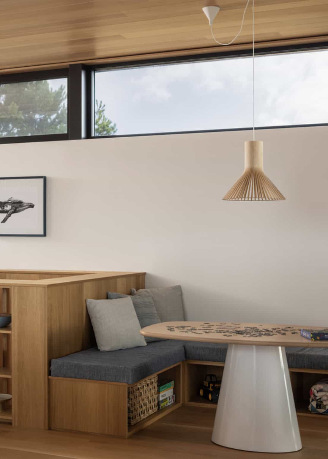 Built-in banquette nook with a puzzle table, wood pendant light, and a bird print on the wall