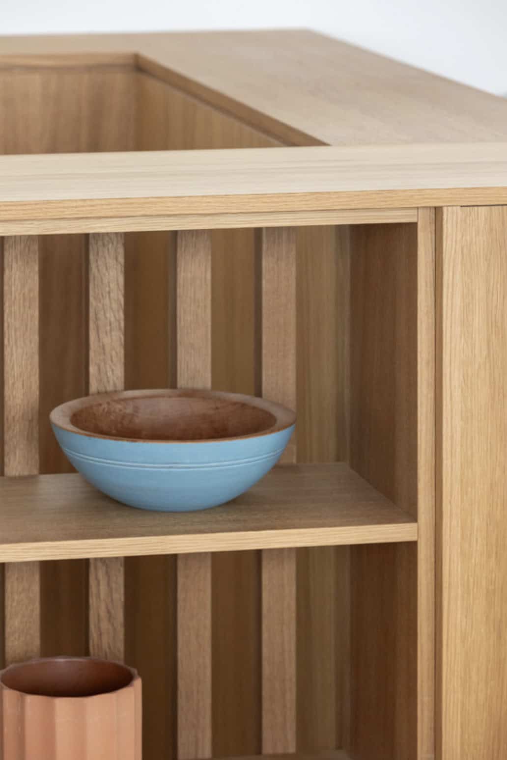 Close-up of a slatted wood shelf holding a blue ceramic bowl and terracotta vase
