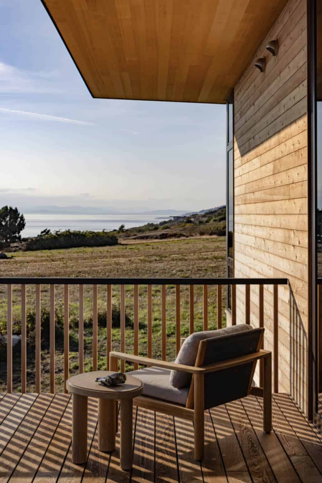 Covered balcony nook with a lounge chair and side table overlooking grassy coastal terrain and the water