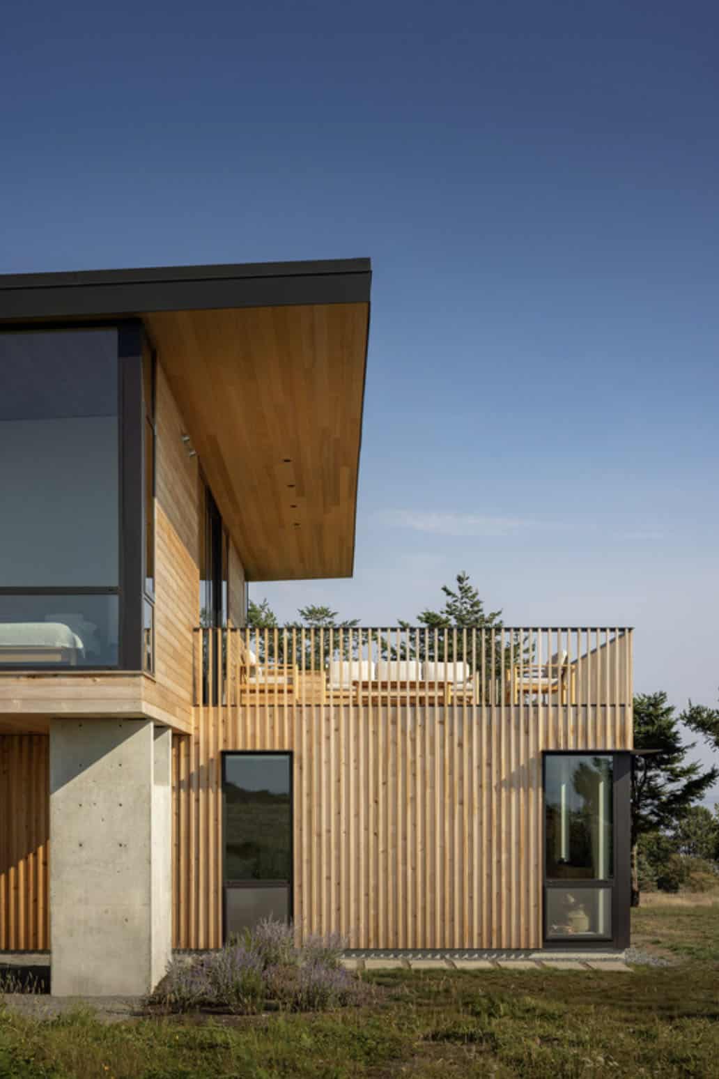 Exterior detail of the cedar-slat upper floor and rooftop deck with seating, set against a clear blue sky