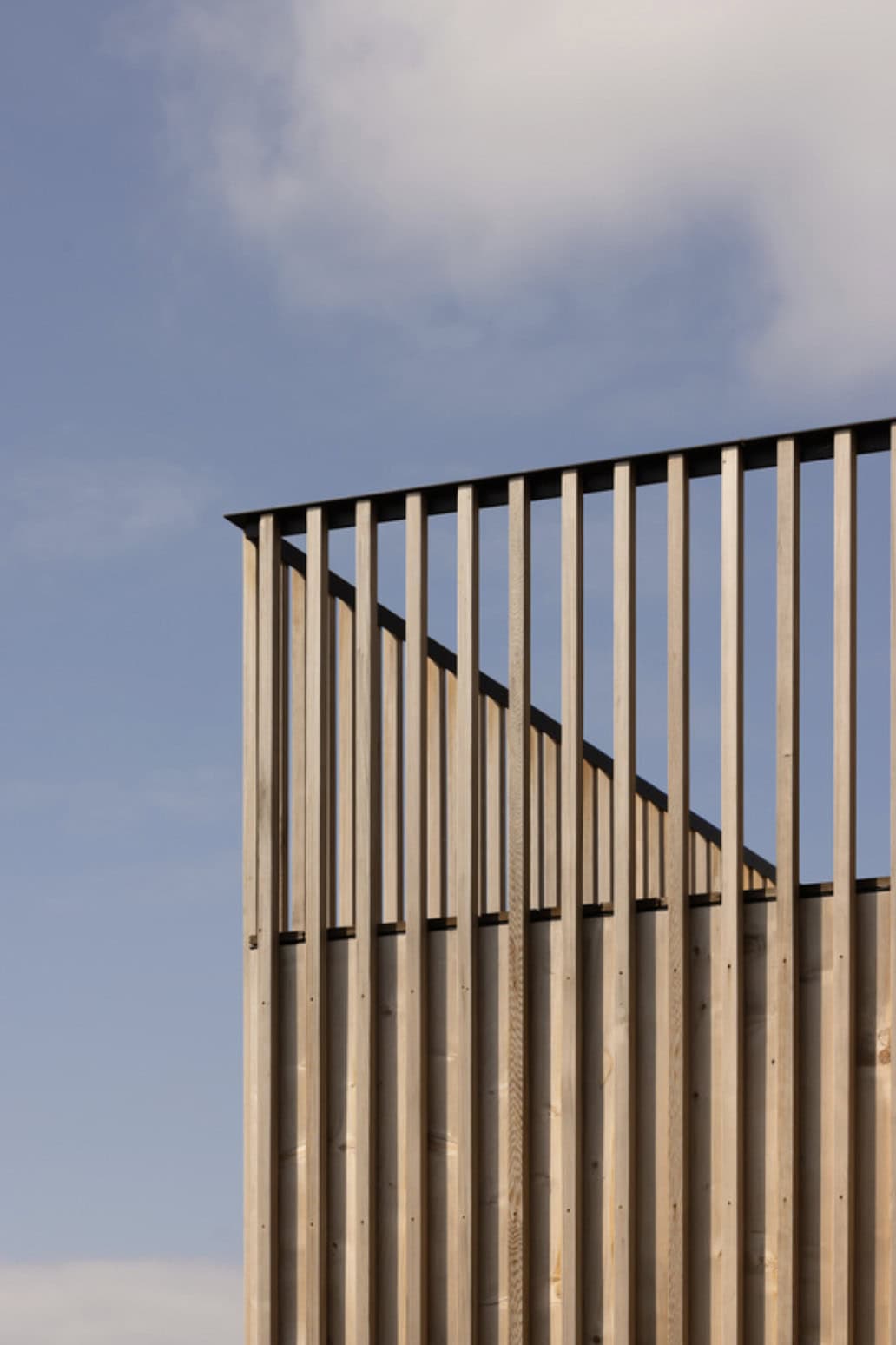 Close-up of angled cedar slat fencing against a partly cloudy sky