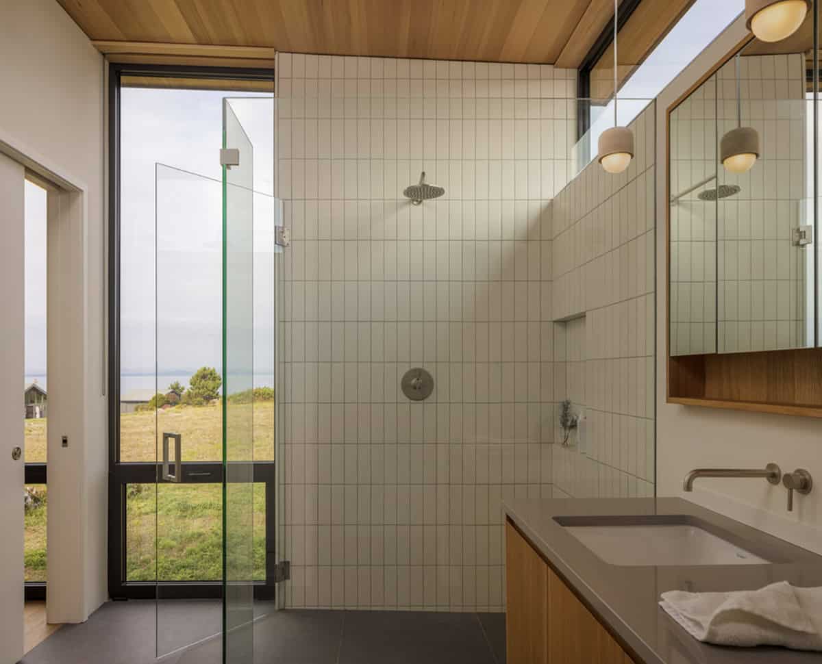 Spa-like bathroom with a glass shower, white tile, ocean-view window, and wood vanity with double sinks