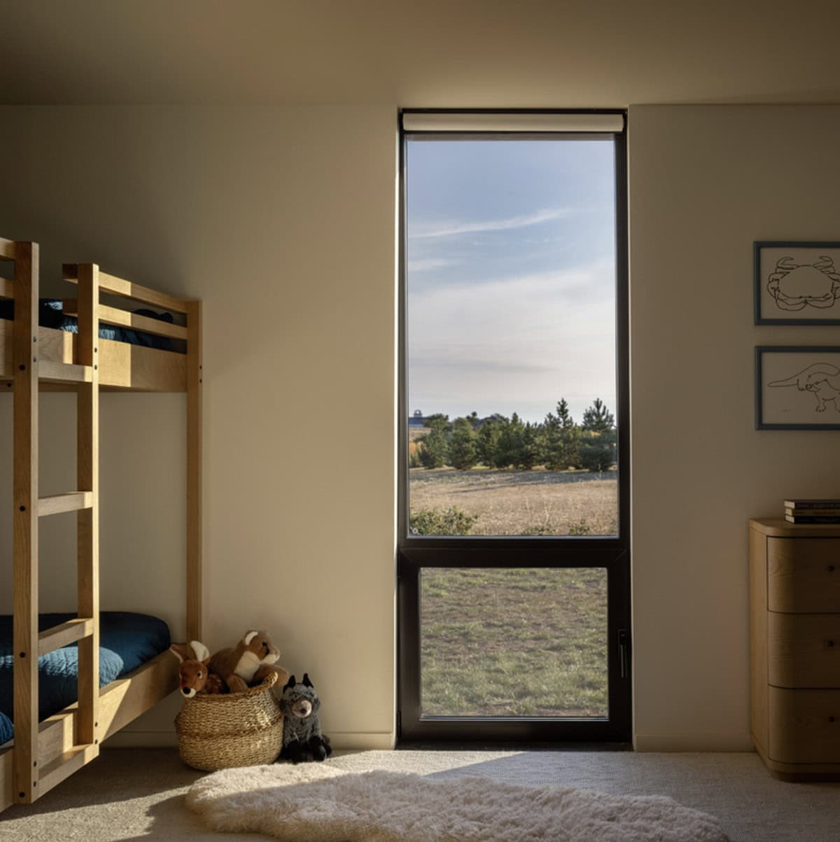 Children's bedroom with a wooden bunk bed, sheepskin rug, plush toys, and a tall window overlooking the fields